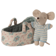 A stuffed toy mouse wearing a blue striped outfit stands beside a small floral-patterned fabric cradle, conveying a playful and cozy atmosphere.