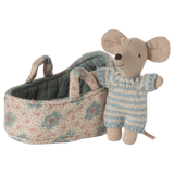 A stuffed toy mouse wearing a blue striped outfit stands beside a small floral-patterned fabric cradle, conveying a playful and cozy atmosphere.