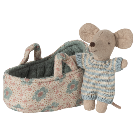 A stuffed toy mouse wearing a blue striped outfit stands beside a small floral-patterned fabric cradle, conveying a playful and cozy atmosphere.