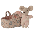 Toy mouse in soft pink knit outfit stands beside a fabric basket with floral patterns. The scene evokes warmth and playfulness.