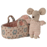 Toy mouse in soft pink knit outfit stands beside a fabric basket with floral patterns. The scene evokes warmth and playfulness.