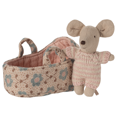 Toy mouse in soft pink knit outfit stands beside a fabric basket with floral patterns. The scene evokes warmth and playfulness.