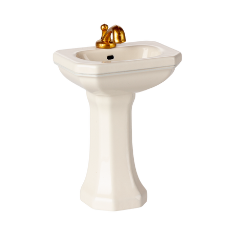 A miniature porcelain pedestal sink with a glossy finish and golden faucet. This elegant bathroom fixture conveys a sense of luxury and vintage charm.