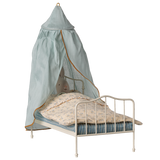 A small white metal bed with a stuffed rabbit under a floral blanket, covered by a light blue canopy with an orange trim, against a white background.