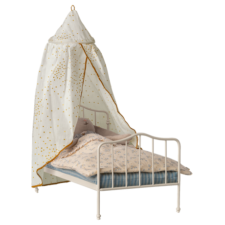 A miniature white metal bed with a blue-striped mattress and floral-patterned bedding. A white canopy with golden spots drapes over, creating a cozy, whimsical feel.