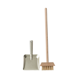 A miniature dustpan with a metal finish and a wooden-handled broom with natural bristles are placed upright on a plain background, evoking simplicity and cleanliness.