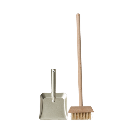 A miniature dustpan with a metal finish and a wooden-handled broom with natural bristles are placed upright on a plain background, evoking simplicity and cleanliness.
