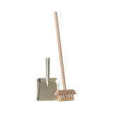 A miniature dustpan with a metal finish and a wooden-handled broom with natural bristles are placed upright on a plain background, evoking simplicity and cleanliness.