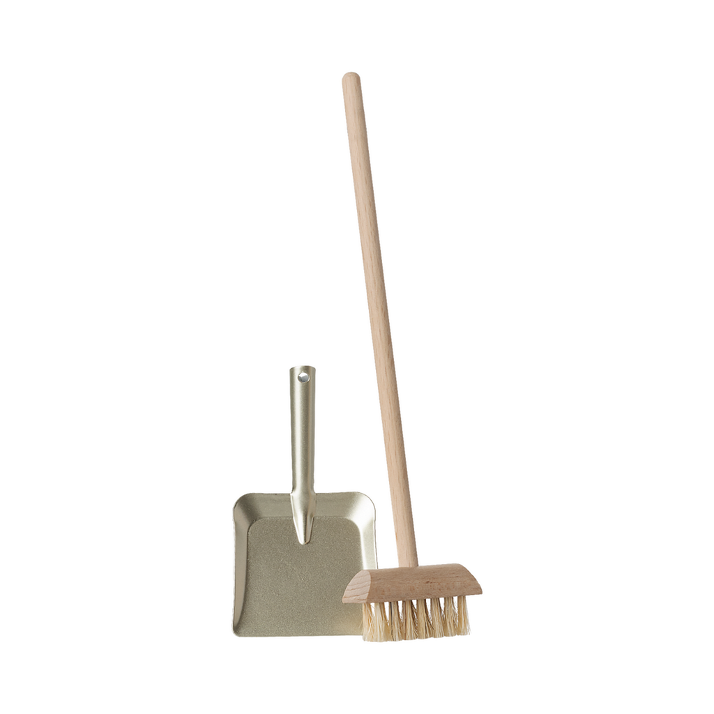 A miniature dustpan with a metal finish and a wooden-handled broom with natural bristles are placed upright on a plain background, evoking simplicity and cleanliness.