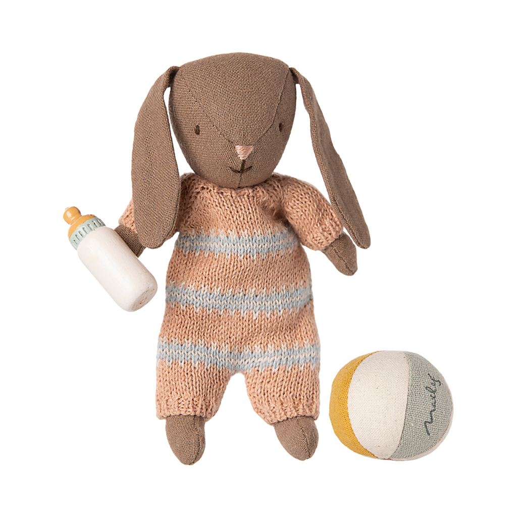 A soft toy bunny with floppy ears wearing a knitted orange and blue striped outfit, holding a baby bottle. A small ball with muted colors is nearby.