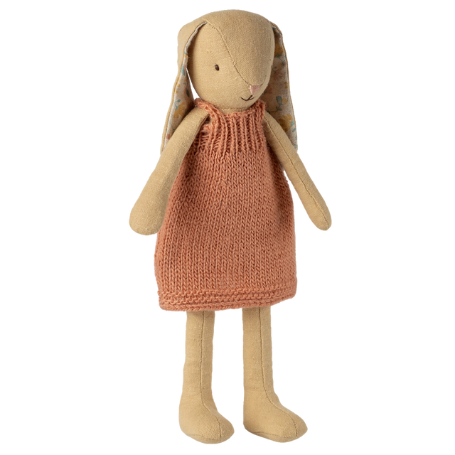 A plush rabbit toy wearing a knitted orange dress stands against a white background. It has long ears, simple stitched features, and a soft, cozy appearance.