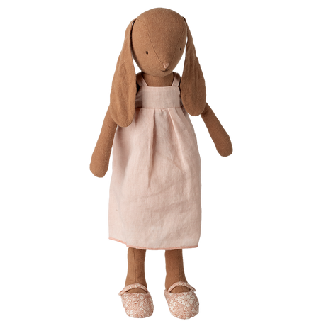 Stuffed rabbit toy with long ears, wearing a light pink dress and floral-patterned shoes, set against a white background, conveying a vintage charm.
