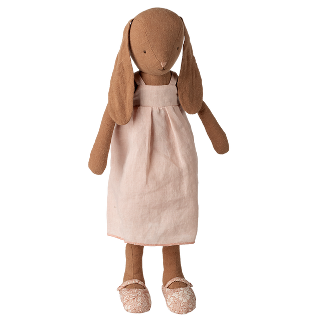 Stuffed rabbit toy with long ears, wearing a light pink dress and floral-patterned shoes, set against a white background, conveying a vintage charm.