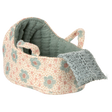 Knitted toy cradle with a floral pattern in pastel blue and blush. A cozy blue blanket drapes over the edge, creating a warm and inviting atmosphere.