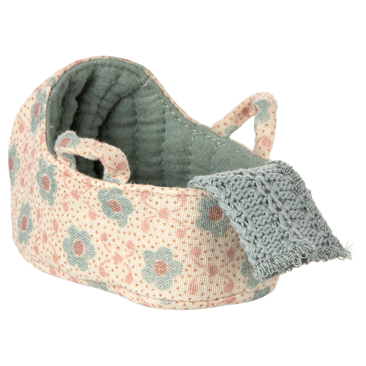 Knitted toy cradle with a floral pattern in pastel blue and blush. A cozy blue blanket drapes over the edge, creating a warm and inviting atmosphere.
