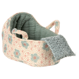 Knitted toy cradle with a floral pattern in pastel blue and blush. A cozy blue blanket drapes over the edge, creating a warm and inviting atmosphere.