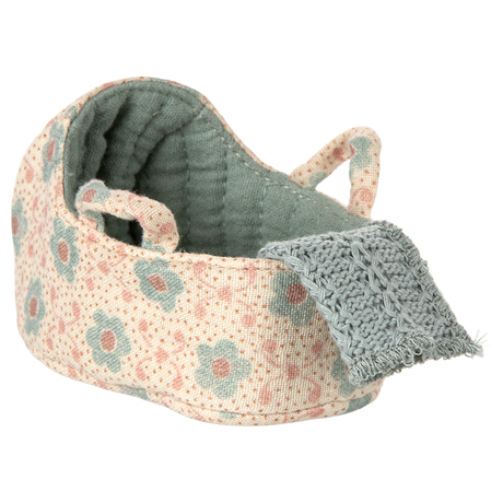 Knitted toy cradle with a floral pattern in pastel blue and blush. A cozy blue blanket drapes over the edge, creating a warm and inviting atmosphere.