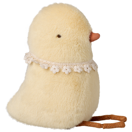 Fluffy yellow chick plush with small orange beak and lace flower collar, on a white background. The chick sits upright, evoking a cute and whimsical tone.