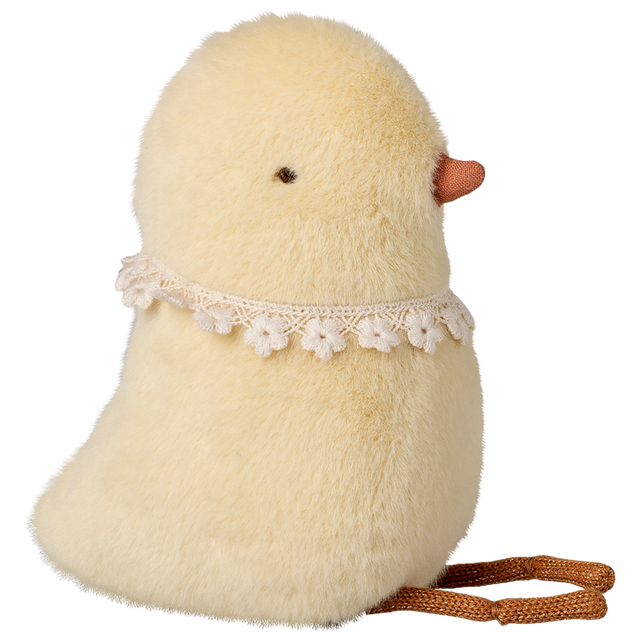Fluffy yellow chick plush with small orange beak and lace flower collar, on a white background. The chick sits upright, evoking a cute and whimsical tone.