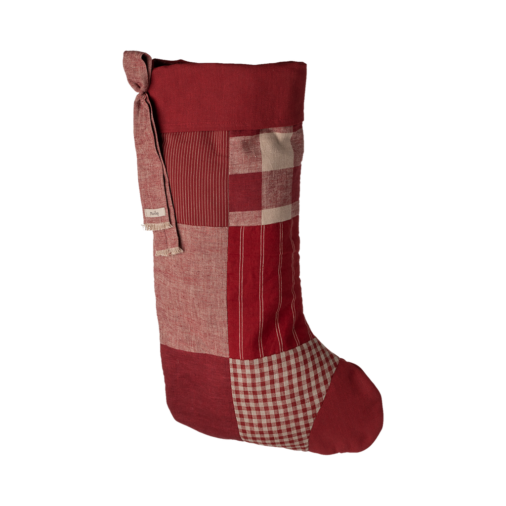 A tall, patchwork holiday stocking in shades of red, featuring various fabric textures and patterns, tied with a decorative knot.