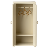 Cream-colored mini wardrobe with open doors, revealing three gold hangers on a rod and a single shelf below. It conveys simplicity and tidiness.
