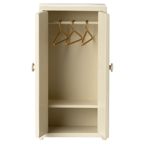 Cream-colored mini wardrobe with open doors, revealing three gold hangers on a rod and a single shelf below. It conveys simplicity and tidiness.
