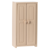 A small, beige, two-door cabinet with simple panel designs and round floral knobs, set against a white background, conveying a minimalist style.
