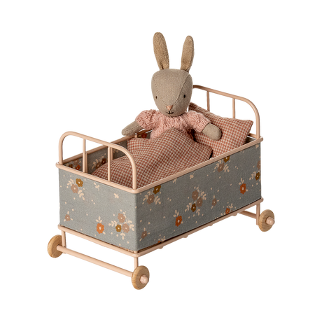 Vintage-style miniature toy crib with floral fabric, soft brown and beige tones. Features small wheels, a houndstooth pillow, and a cozy blanket, evoking a nostalgic charm.