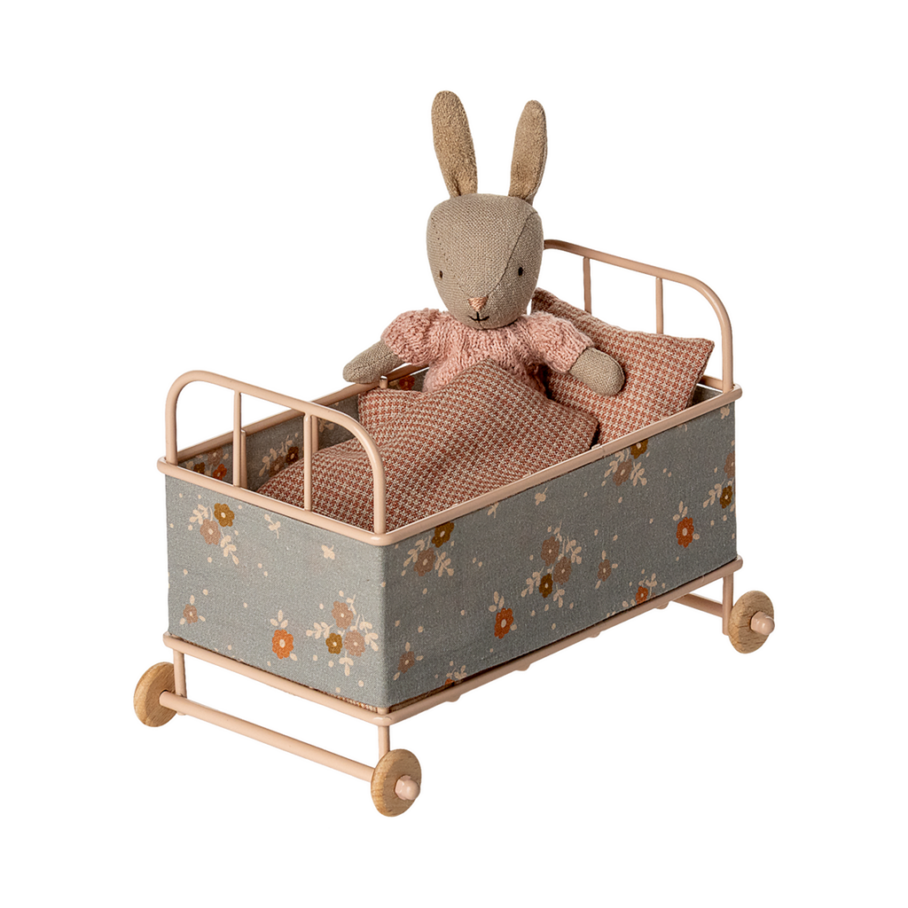 Vintage-style miniature toy crib with floral fabric, soft brown and beige tones. Features small wheels, a houndstooth pillow, and a cozy blanket, evoking a nostalgic charm.