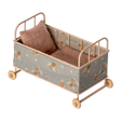 Vintage-style miniature toy crib with floral fabric, soft brown and beige tones. Features small wheels, a houndstooth pillow, and a cozy blanket, evoking a nostalgic charm.