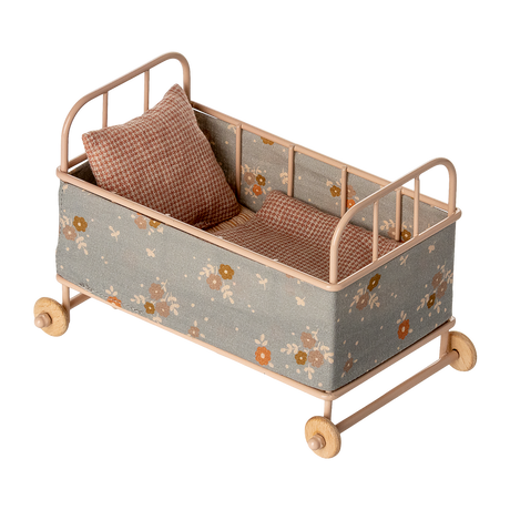 Vintage-style miniature toy crib with floral fabric, soft brown and beige tones. Features small wheels, a houndstooth pillow, and a cozy blanket, evoking a nostalgic charm.