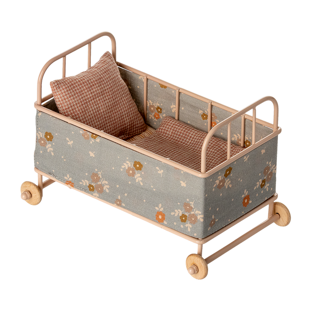 Vintage-style miniature toy crib with floral fabric, soft brown and beige tones. Features small wheels, a houndstooth pillow, and a cozy blanket, evoking a nostalgic charm.