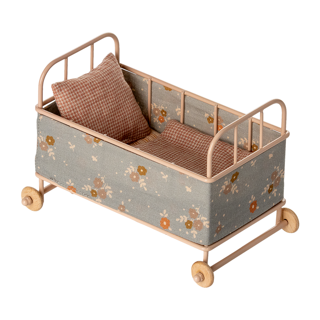 Vintage-style miniature toy crib with floral fabric, soft brown and beige tones. Features small wheels, a houndstooth pillow, and a cozy blanket, evoking a nostalgic charm.