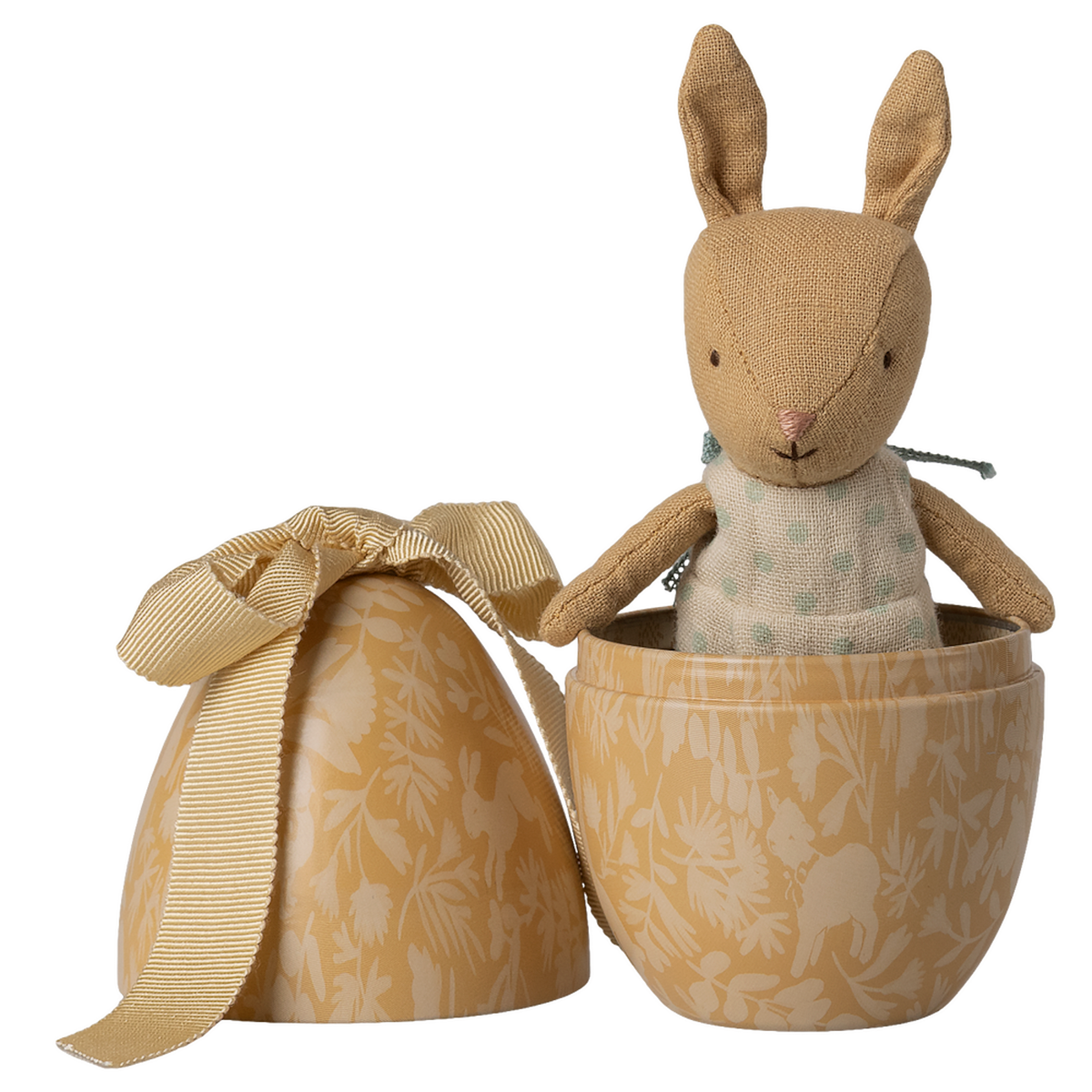 A small, brown plush bunny wearing a polka-dotted outfit sits inside an open, decorative beige egg with floral patterns and a ribbon, against a white background.