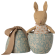A stuffed bunny in a polka-dot dress peeks out of a decorative blue egg-shaped container with floral patterns and a tied beige ribbon.