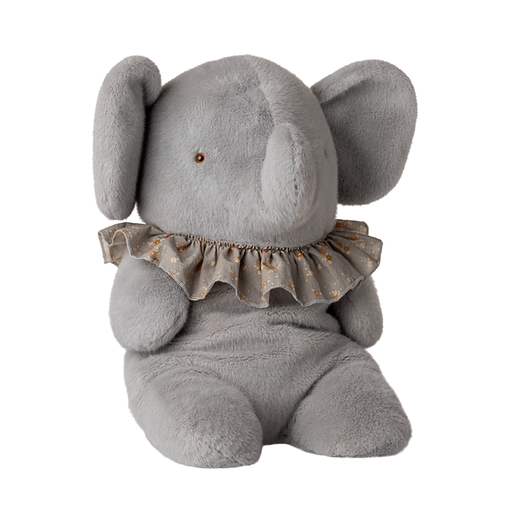 A plush gray elephant toy with large ears and a small brown eye sits wearing a ruffled collar with a floral pattern. The toy conveys a cozy, playful vibe.