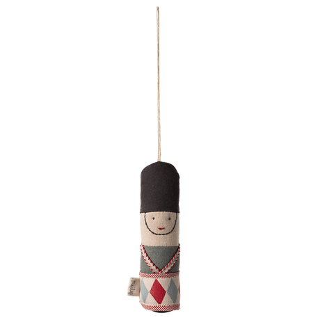 Cloth toy soldier ornament with a black hat, embroidered face, and patterned uniform hangs from a string against a white background.