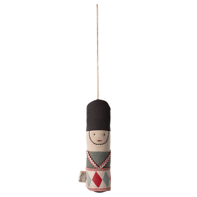Cloth toy soldier ornament with a black hat, embroidered face, and patterned uniform hangs from a string against a white background.