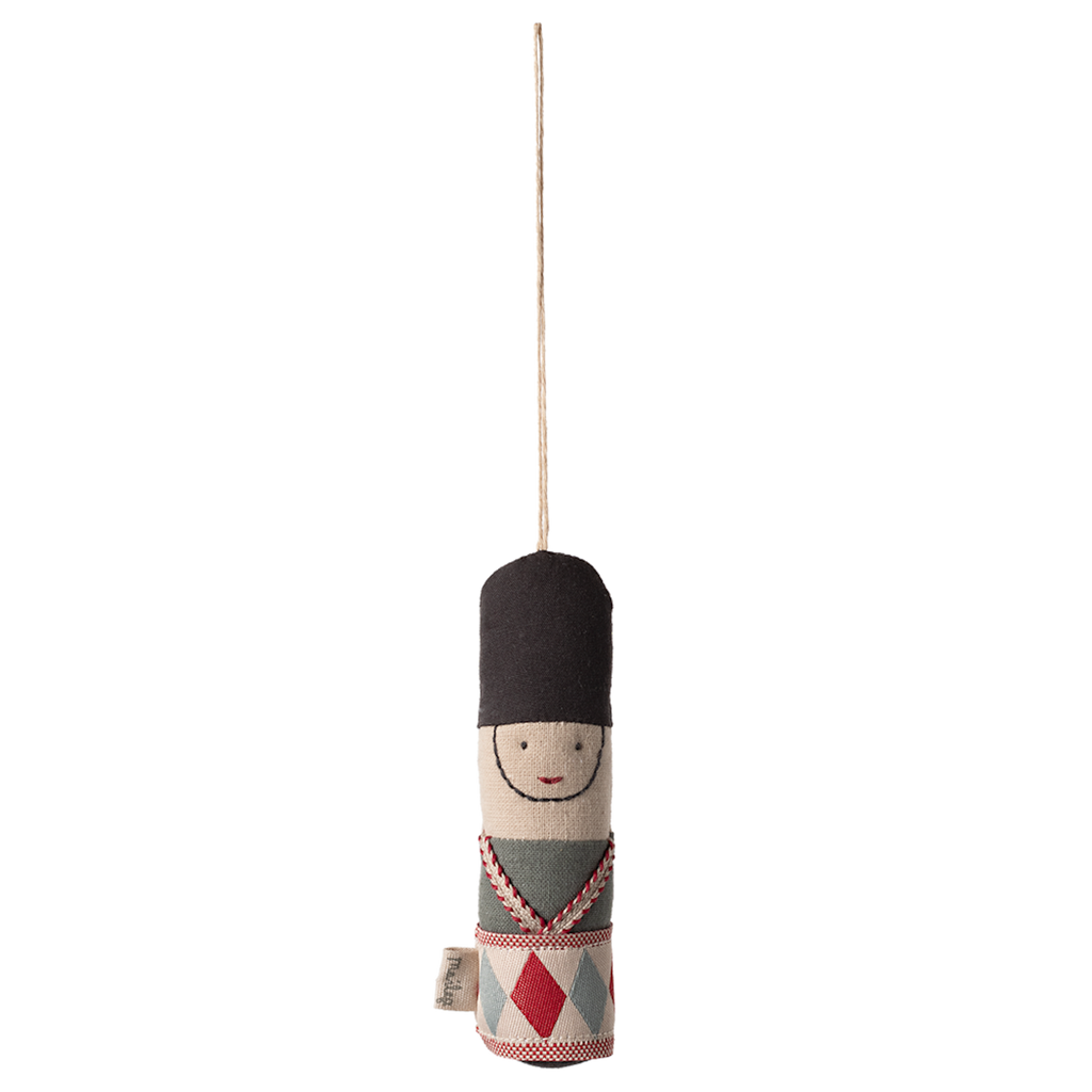 Cloth toy soldier ornament with a black hat, embroidered face, and patterned uniform hangs from a string against a white background.