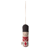 A hanging ornament depicting a smiling toy soldier with a tall black hat and red, blue, and white uniform, set against a white background.