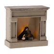 Miniature off-white dollhouse fireplace with a pile of faux logs glowing with a warm orange light.