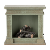 A decorative miniature fireplace with a greenish-gray finish, holding several stacked logs inside, showcasing a cozy and rustic vibe.