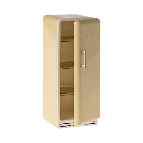 A toy refrigerator in a pale yellow color, is shown with its door slightly ajar. The fridge has a retro design with rounded edges, a silver-colored handle on the right side of the door, and the word "MAILEG" embossed vertically on the door. Inside, three shelves with ribbed textures are visible.