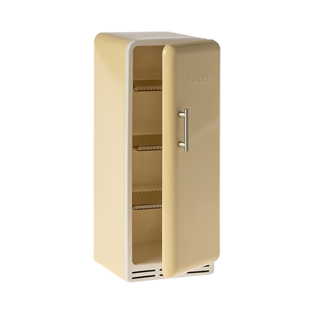 A toy refrigerator in a pale yellow color, is shown with its door slightly ajar. The fridge has a retro design with rounded edges, a silver-colored handle on the right side of the door, and the word "MAILEG" embossed vertically on the door. Inside, three shelves with ribbed textures are visible.