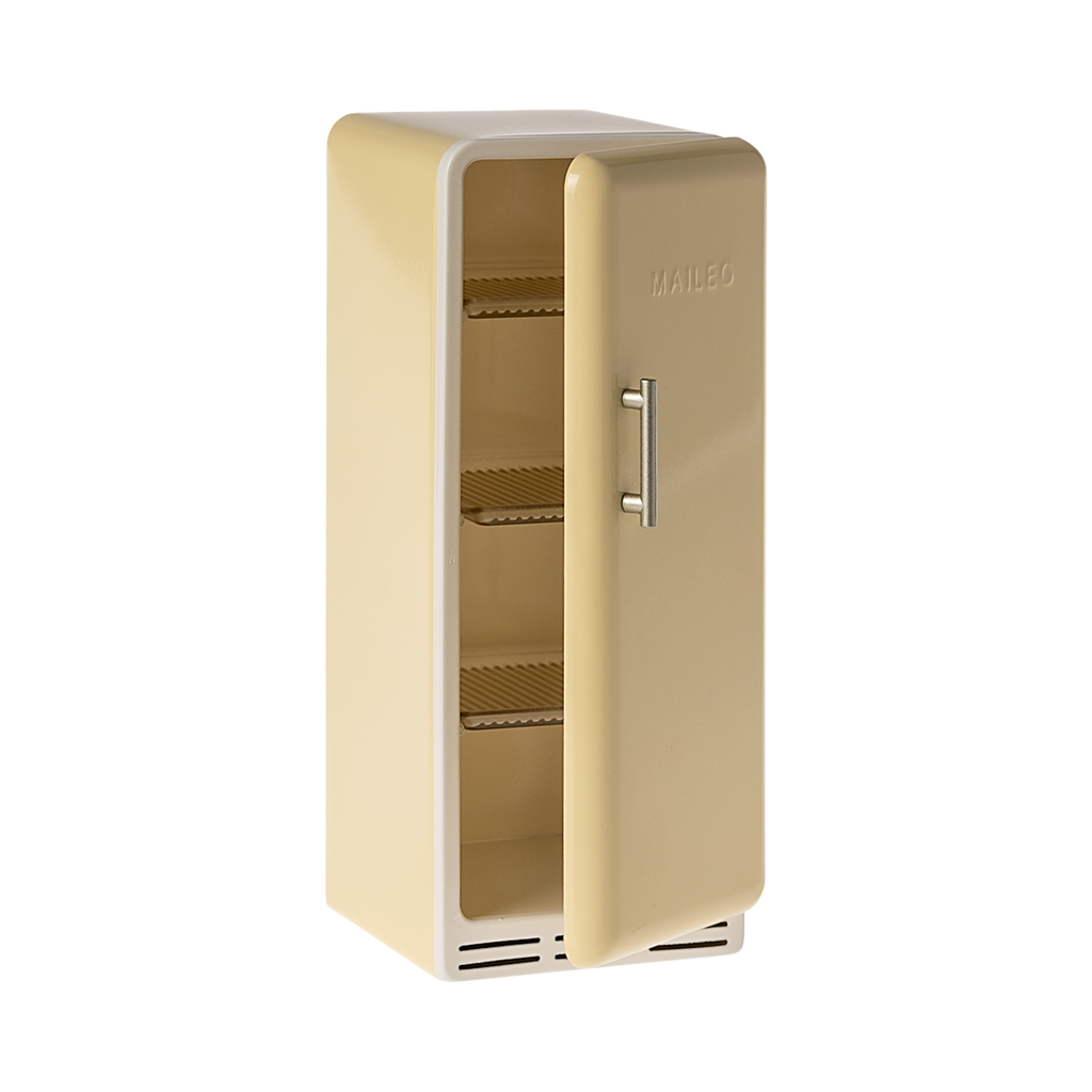 A toy refrigerator in a pale yellow color, is shown with its door slightly ajar. The fridge has a retro design with rounded edges, a silver-colored handle on the right side of the door, and the word "MAILEG" embossed vertically on the door. Inside, three shelves with ribbed textures are visible.