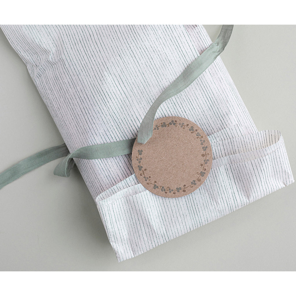 A neatly wrapped gift in striped white paper with a green ribbon and round, brown tag featuring floral patterns on a gray surface. Simple and elegant.