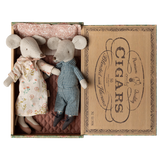 Two fabric mice dolls, one in a floral dress and the other in checkered overalls, lie in a vintage cigar box lined with patterned cloth. Cozy and charming.
