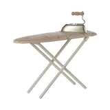 A miniature, foldable ironing board with a floral-patterned surface and a vintage-style iron featuring a wooden handle, set against a plain background.