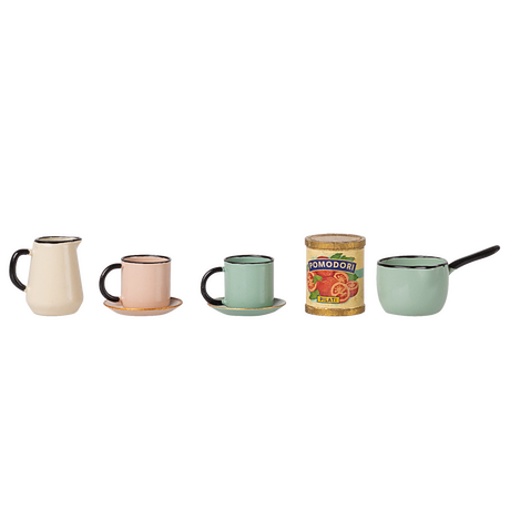 A row of miniature vintage kitchenware: cream pitcher, pink cup with saucer, green cup with saucer, can of tomatoes, and a green saucepan with a handle. Retro vibe.