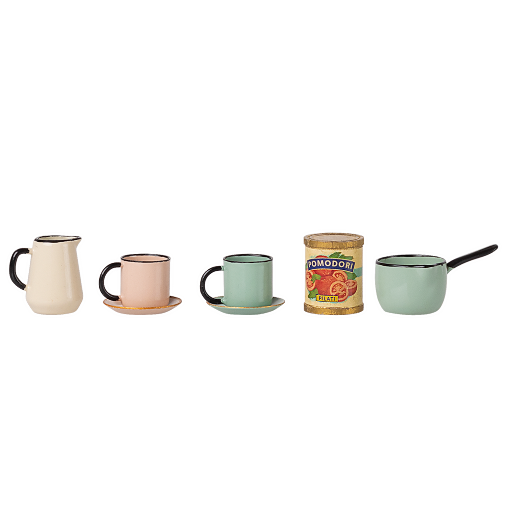 A row of miniature vintage kitchenware: cream pitcher, pink cup with saucer, green cup with saucer, can of tomatoes, and a green saucepan with a handle. Retro vibe.